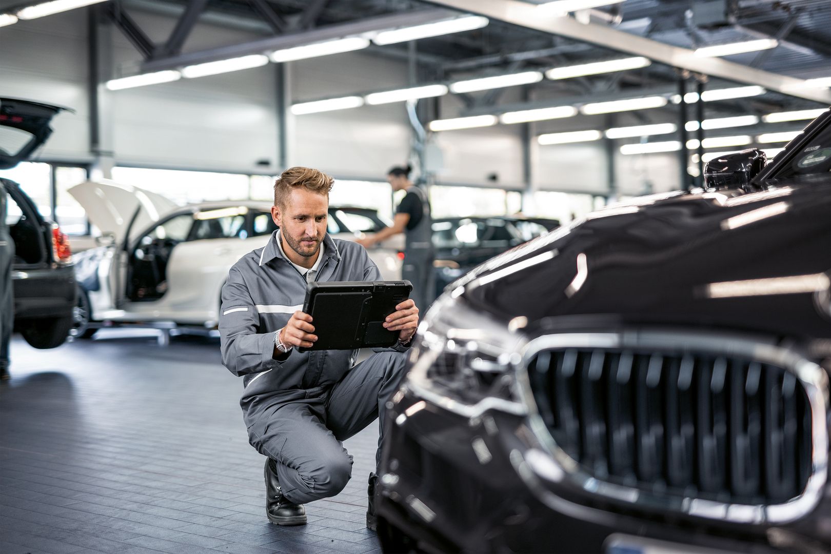 Mechaniker, der in einer Autowerkstatt ein Tablet zur Diagnose eines Autos verwendet