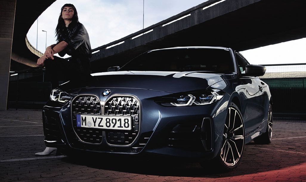Eine junge Frau sitzt auf der Motorhaube eines eleganten, dunkelblauen BMW, der unter einer Überführung geparkt ist